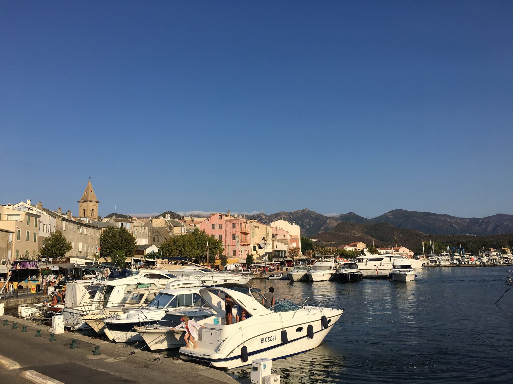 GR Stories | Boats in the harbour of Saint-Florent, with the old town and the mountains behind