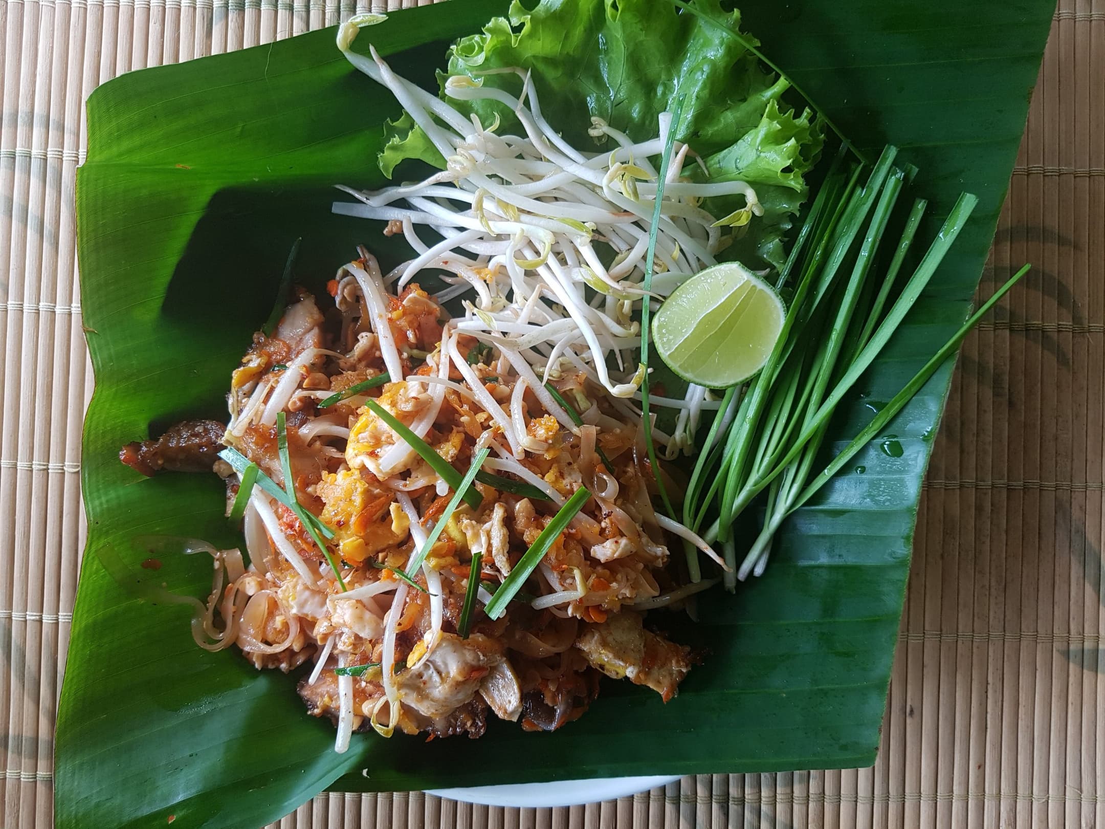 GR Stories | A plate of pad thai on a banana leaf with bean sprouts, garlic chives and lime