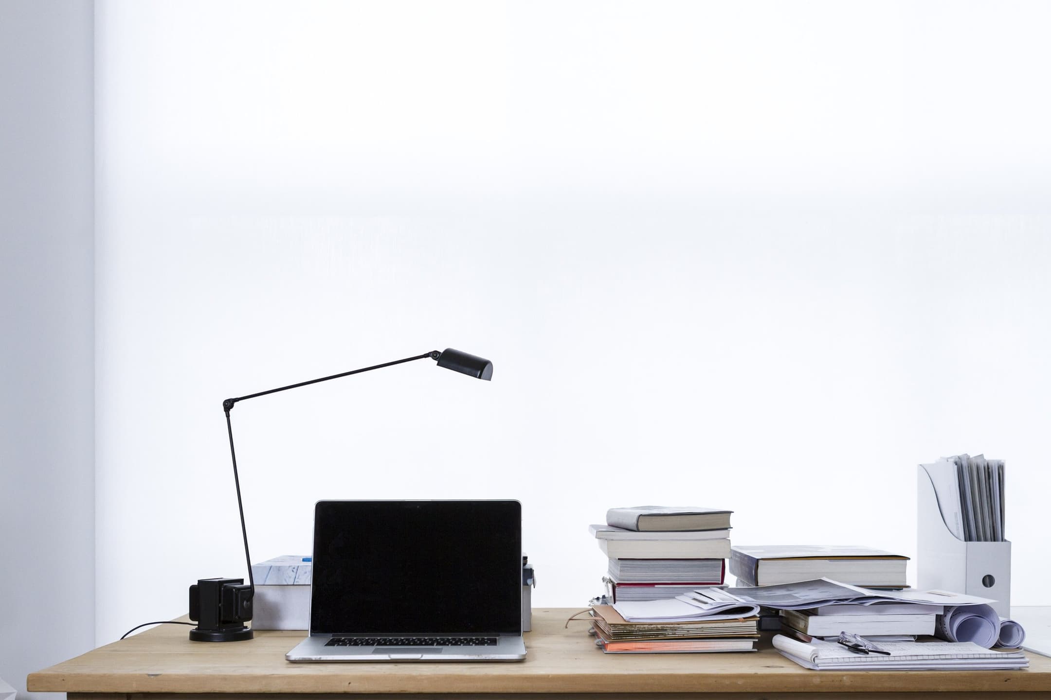 GR Stories | A laptop on a white desk next to stacks of books and a desk lamp